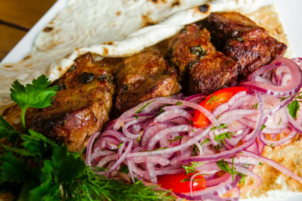 Close-up of grilled meat with herbs and onions on flatbread for a mouth-watering dish.